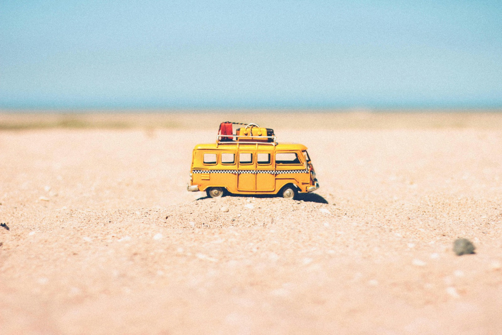 Zandgrond met daarop een close-up van een kleine gele camper.