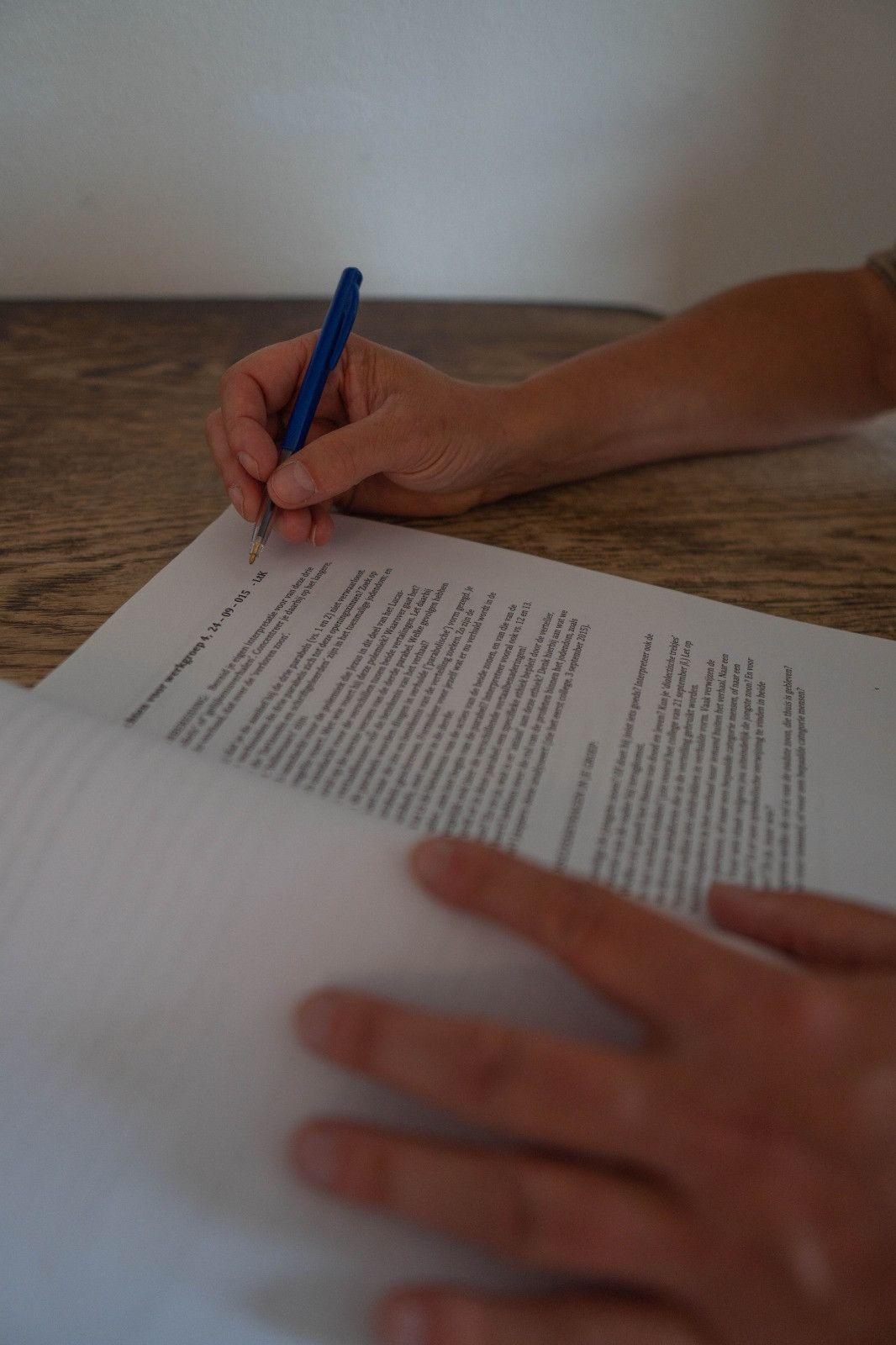 Iemand schrijft met blauwe pen iets in een document. Andere hand ligt op het papier.