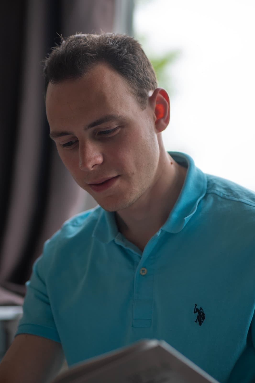 Jongen met bruin haar en lichtblauwe polo aan kijkt in een boek dat hij in zijn handen heeft.