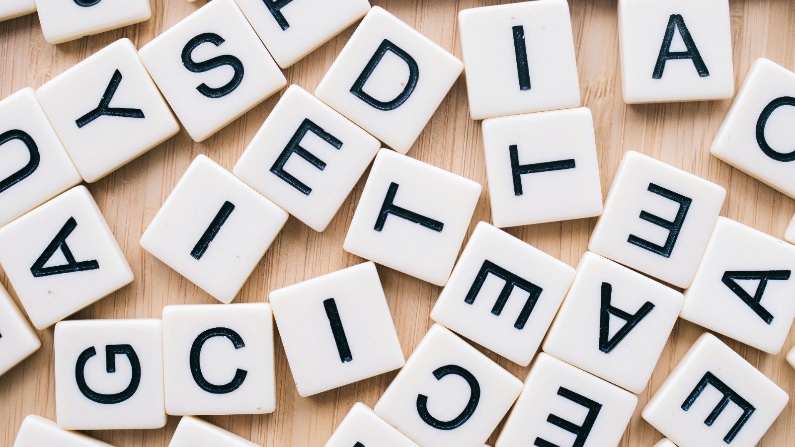 Letterblokjes (zoals Scrabble) liggen door elkaar heen op een houten ondergrond.