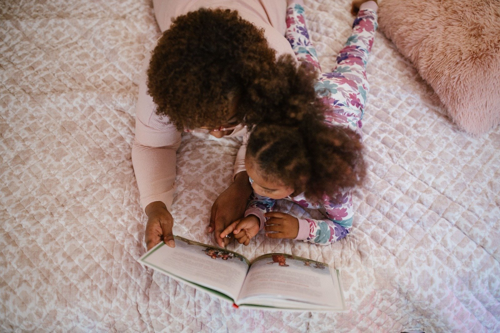 Een oudere dame en jong meisje liggen samen op een zacht kleed en lezen in een boek, het lijkt op moeder en dochter.